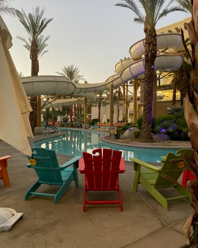 Blue, red and green lounge chairs placed in front of a swimming pool, water slide and palm trees