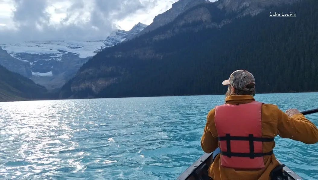 A man canoeing on a lake surrounded by mountains.