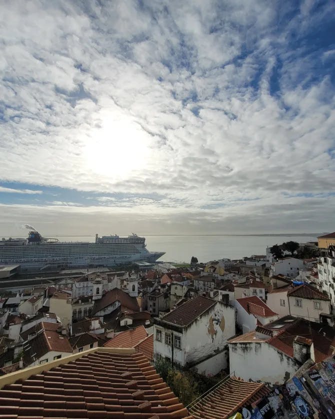 An aerial view of Lisbon with a cruise ship, water and cloudy blue sky in the distance