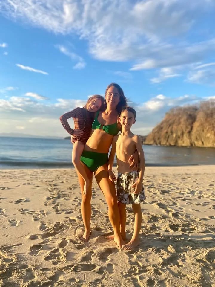 Travel advisor Lauren and children posing in swimsuits on a sandy beach.