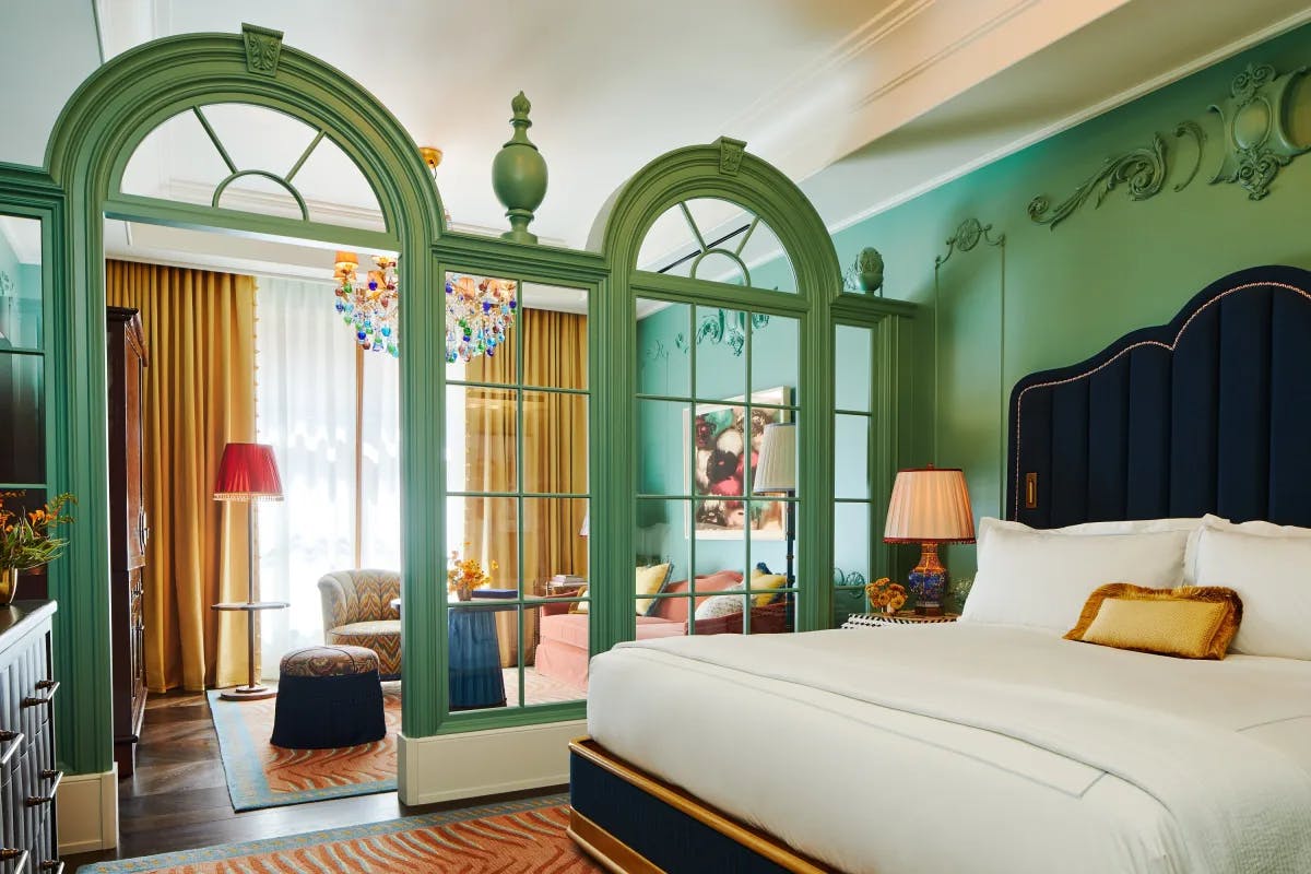 a bright hotel room with green walls, colorful furniture and a sitting area separated from the bedroom by a glass arched divider