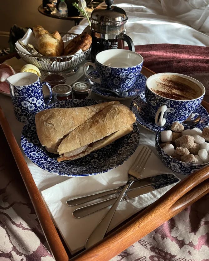 bread, coffee in blue mugs, and sugar cubes on a tray in bed