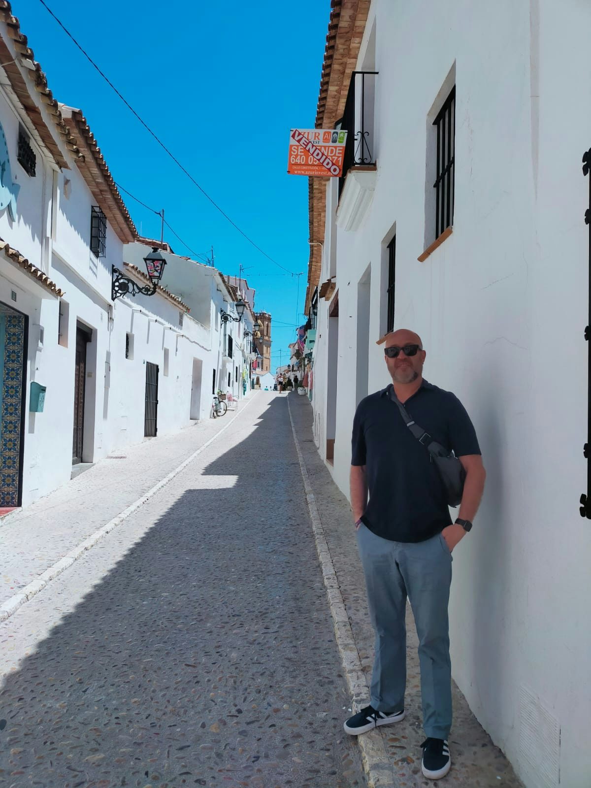 Travel Advisor James Joseph Sterrett Alarcon stands on the stone sidewalk of a street surrounded by white buildingd under a bright blue sky