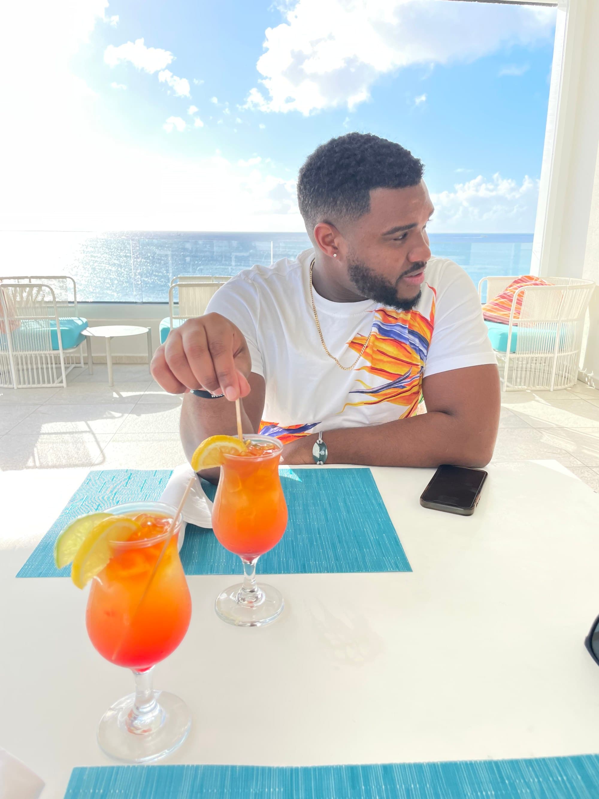 Travel advisor having orange drink with sea in the background.
