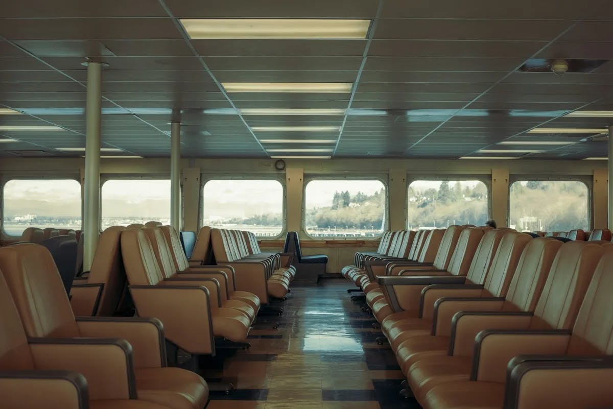 Lounge seating on the Washington Ferry leads up to large bay windows with a view of the pine forested coastline