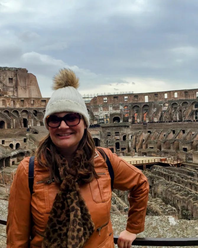 Jamie wearing an orange jacket and winter hat while posing in front of the colosseum in Rome, Italy