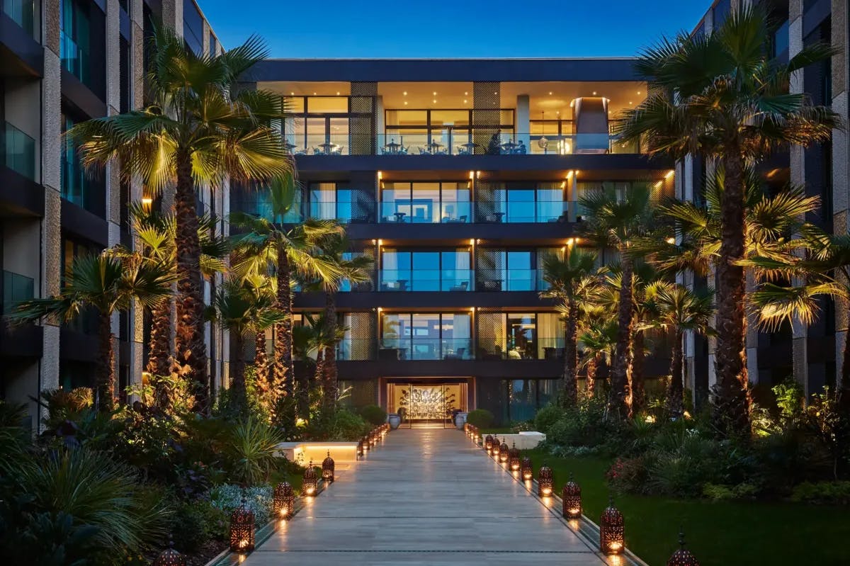 A Moroccan lantern-lit walkway surrounded by palm gardens approaches the courtyard entrance to Four Seasons' Casblanca hotel