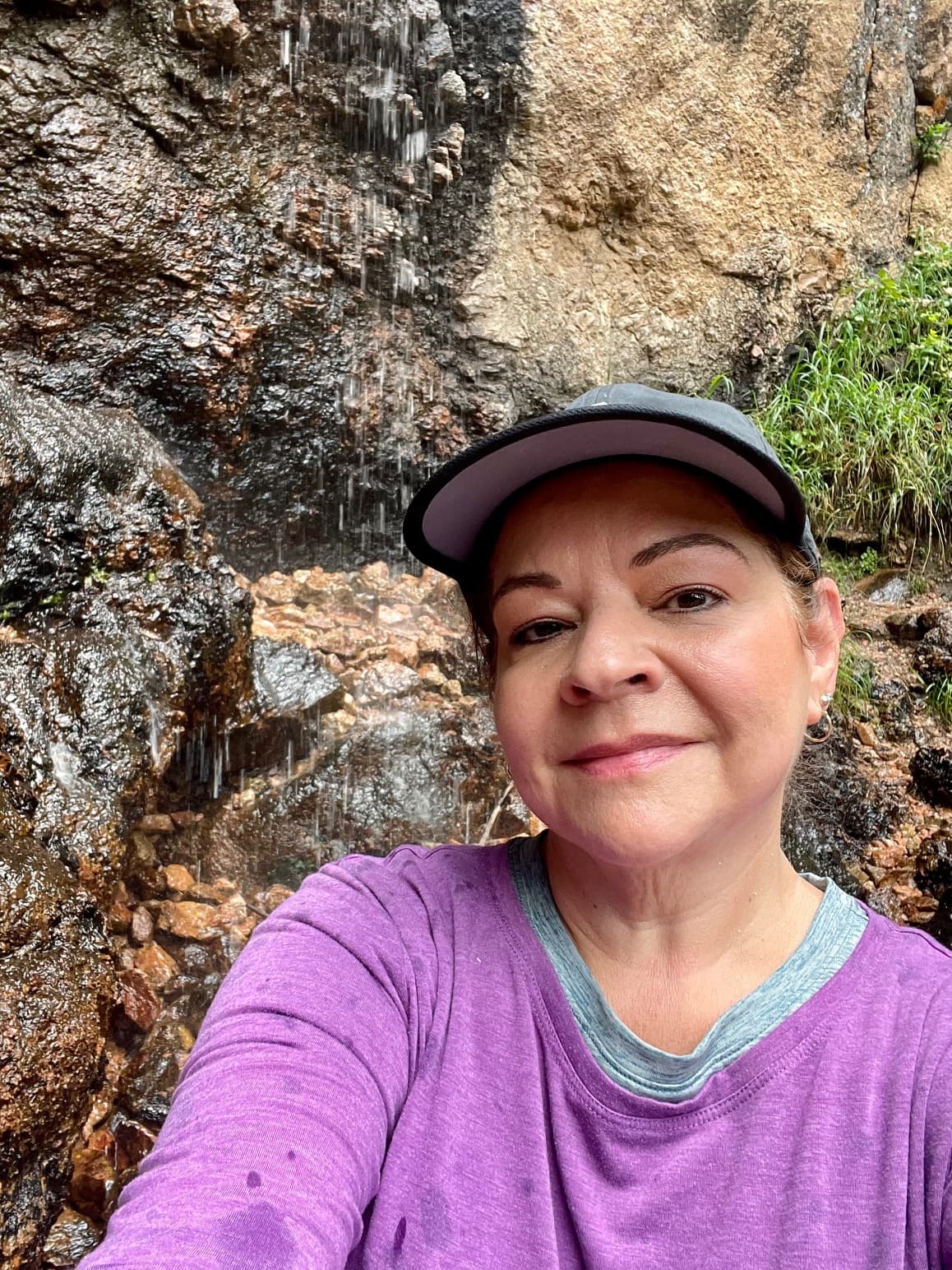Jamie pausing for a photo during a hike, with water dripping down the side of a stone mountain behind her.