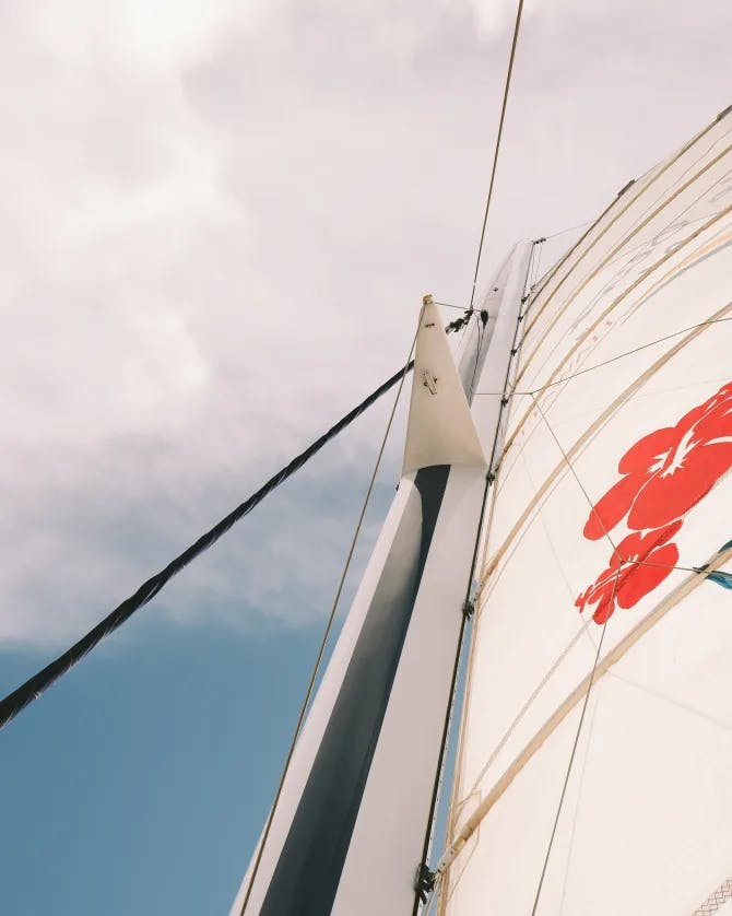 View of a sail on a sail boat with a red design and a cloudy blue sky in the background