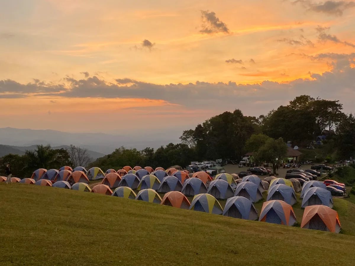 A serene sunset at a campsite with tents pitched on a grassy hill, under a sky painted with warm hues.