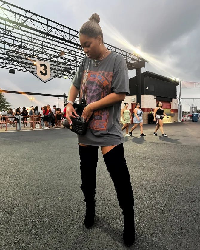Tyler wearing a grey shirt and thigh-high black boots outside at a music venue.
