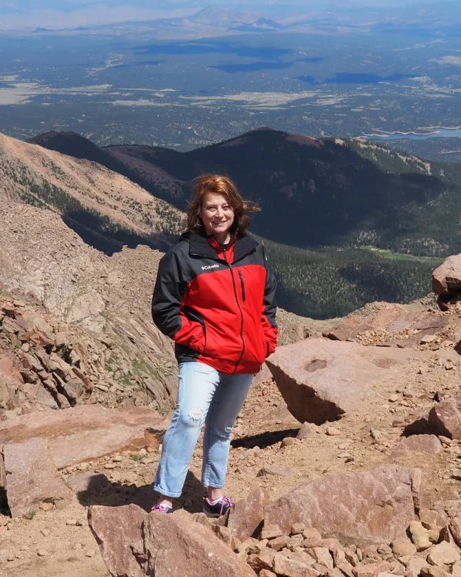 travel advisor Ann Pappas wears a red jacket at the summit of a mountain range