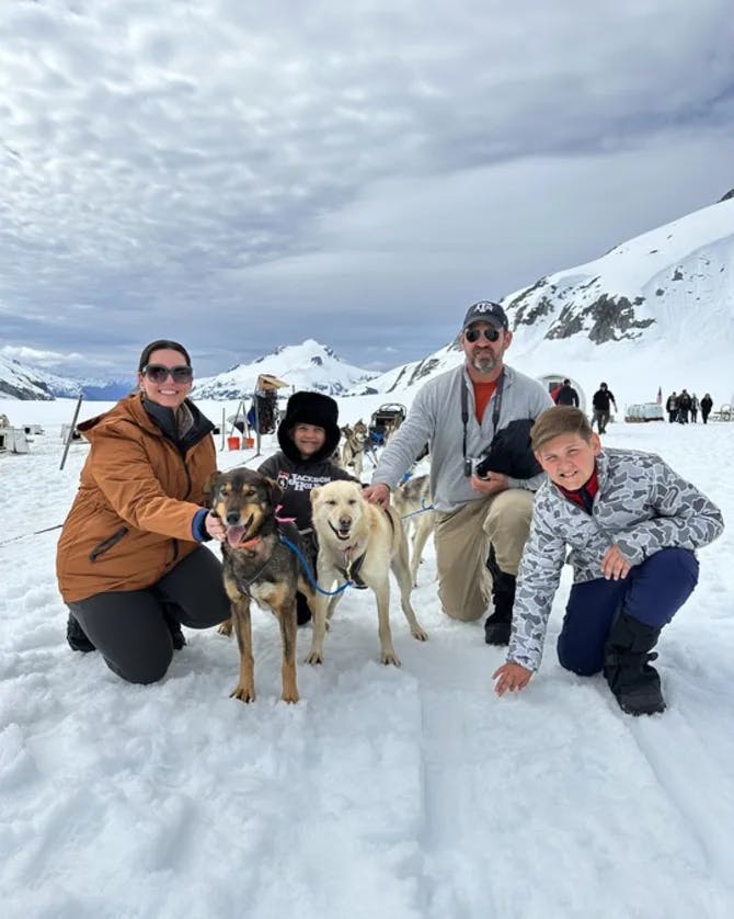 Kimberlie and family posing with dogs outside in the snow with snowy mountains in the background.