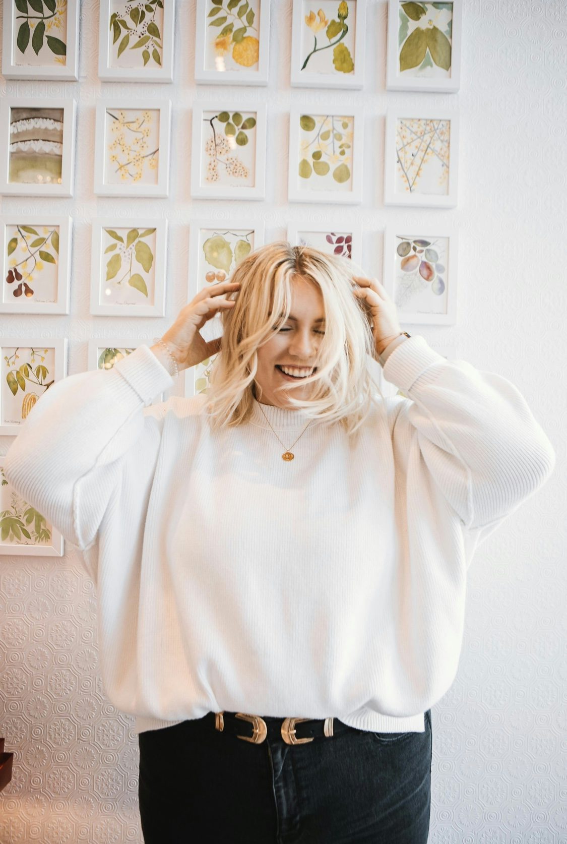 woman wearing a white sweater with a wall of art in the background