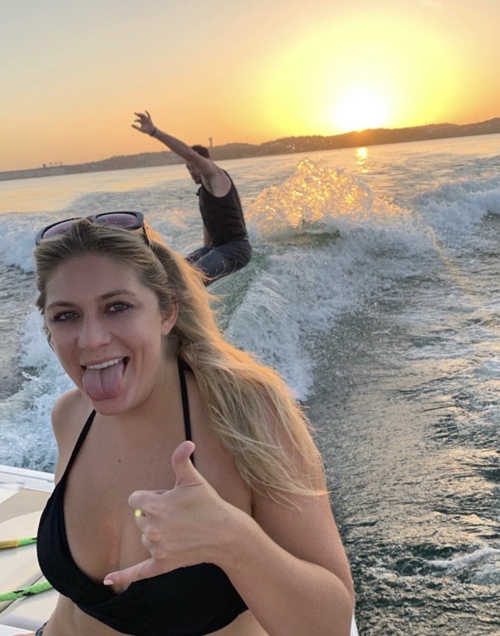 Travel Advisor Stephanie Kelly sits on the back of a boat while a waterskiier rides behind her in the sunset