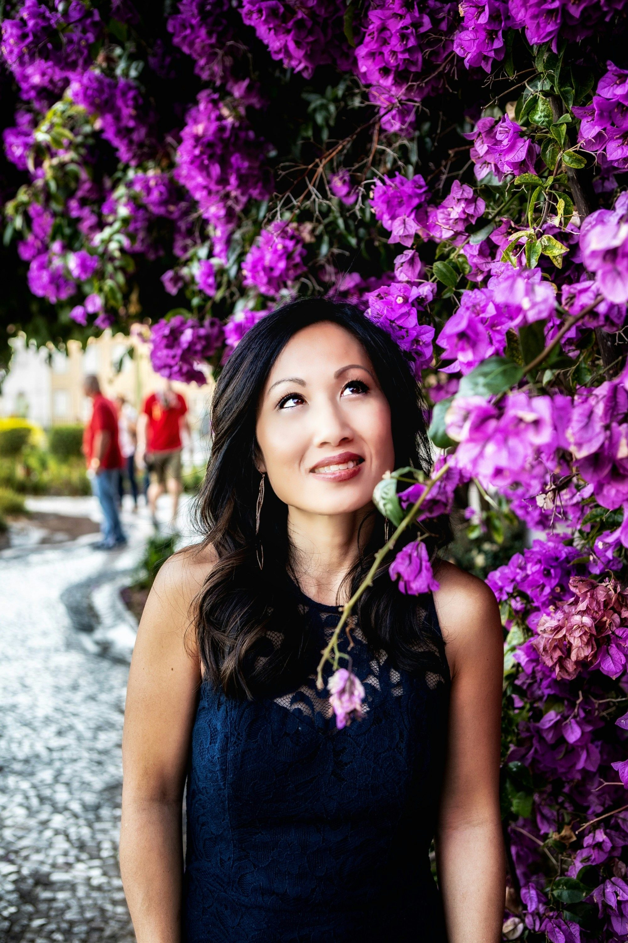 travel advisor Christine Moghadam in a black dress in front of a hedge of purple flowers