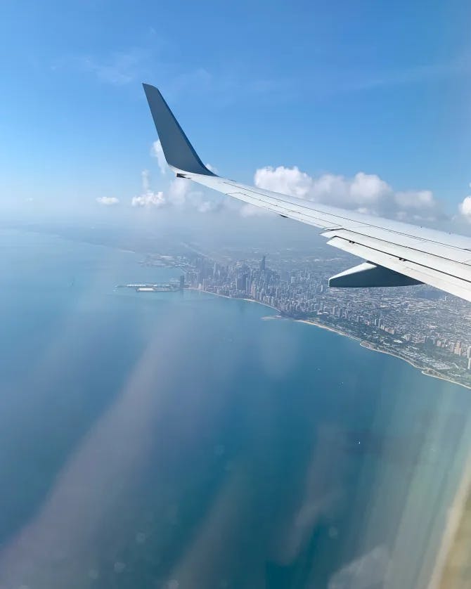 A view of an airplane wing flying over a body of water and costal land.