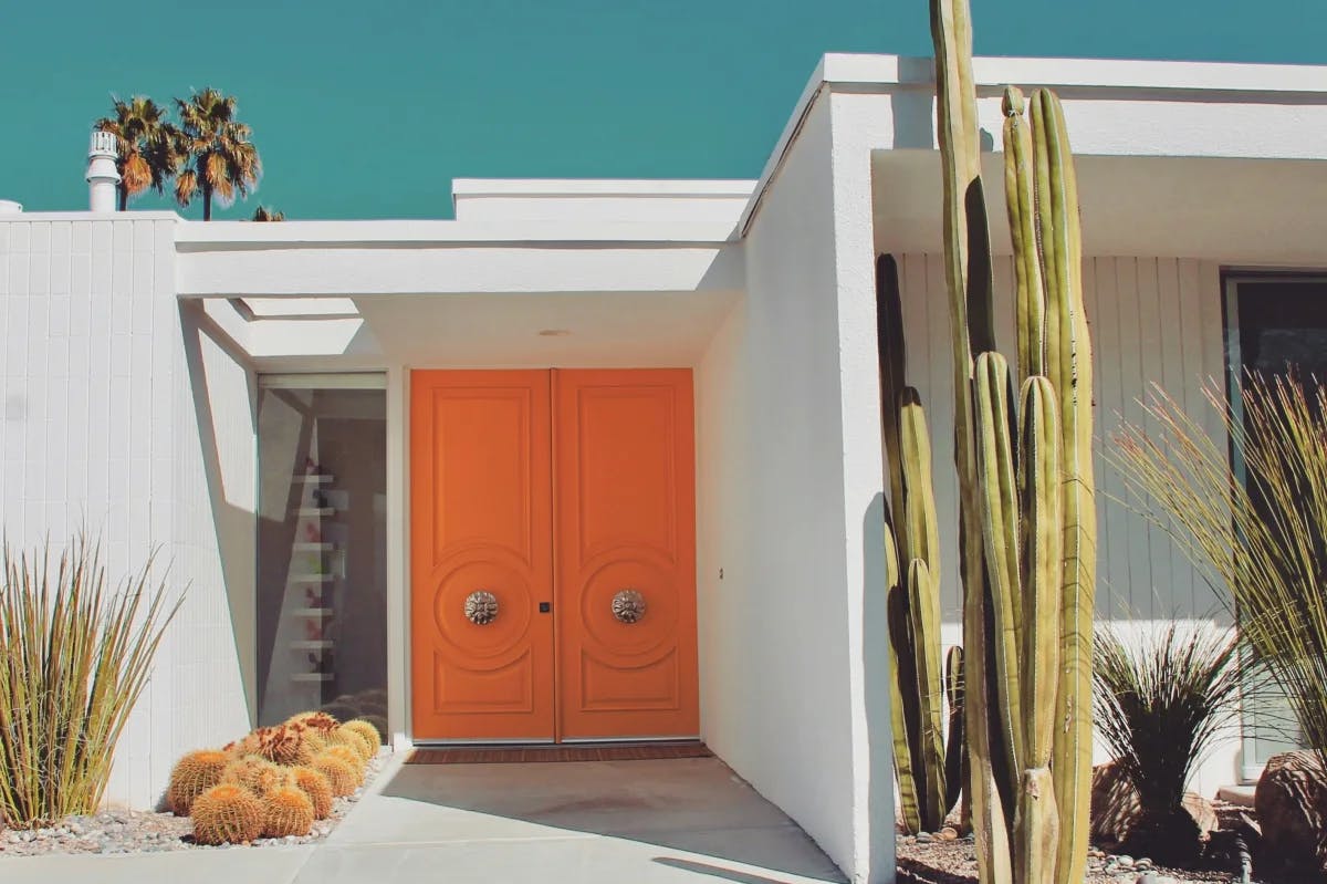 cacti in front of a squat white home with a bright-orange door
