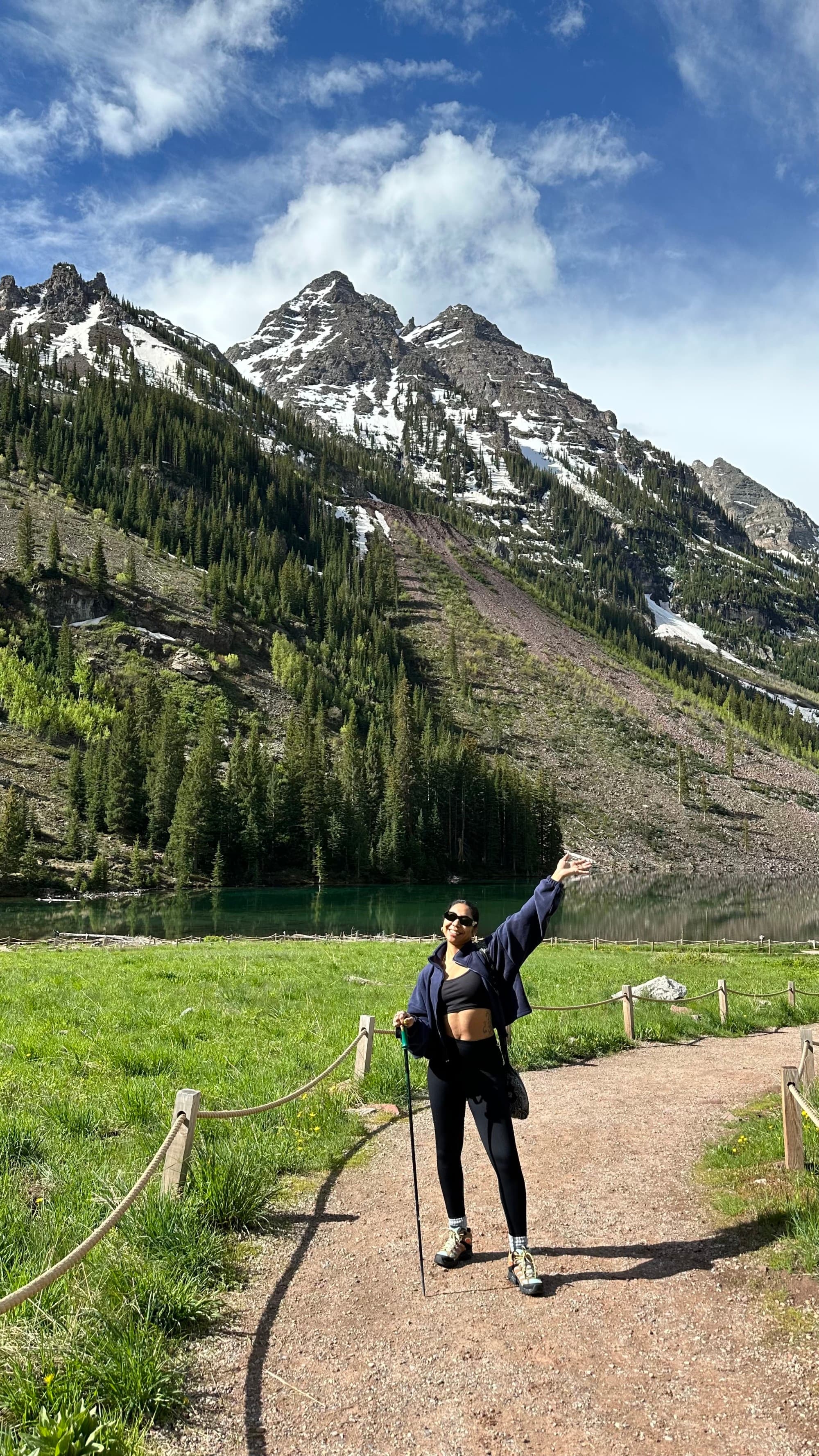 Travel advisor stands at the grassy base of 3 snow topped mountains