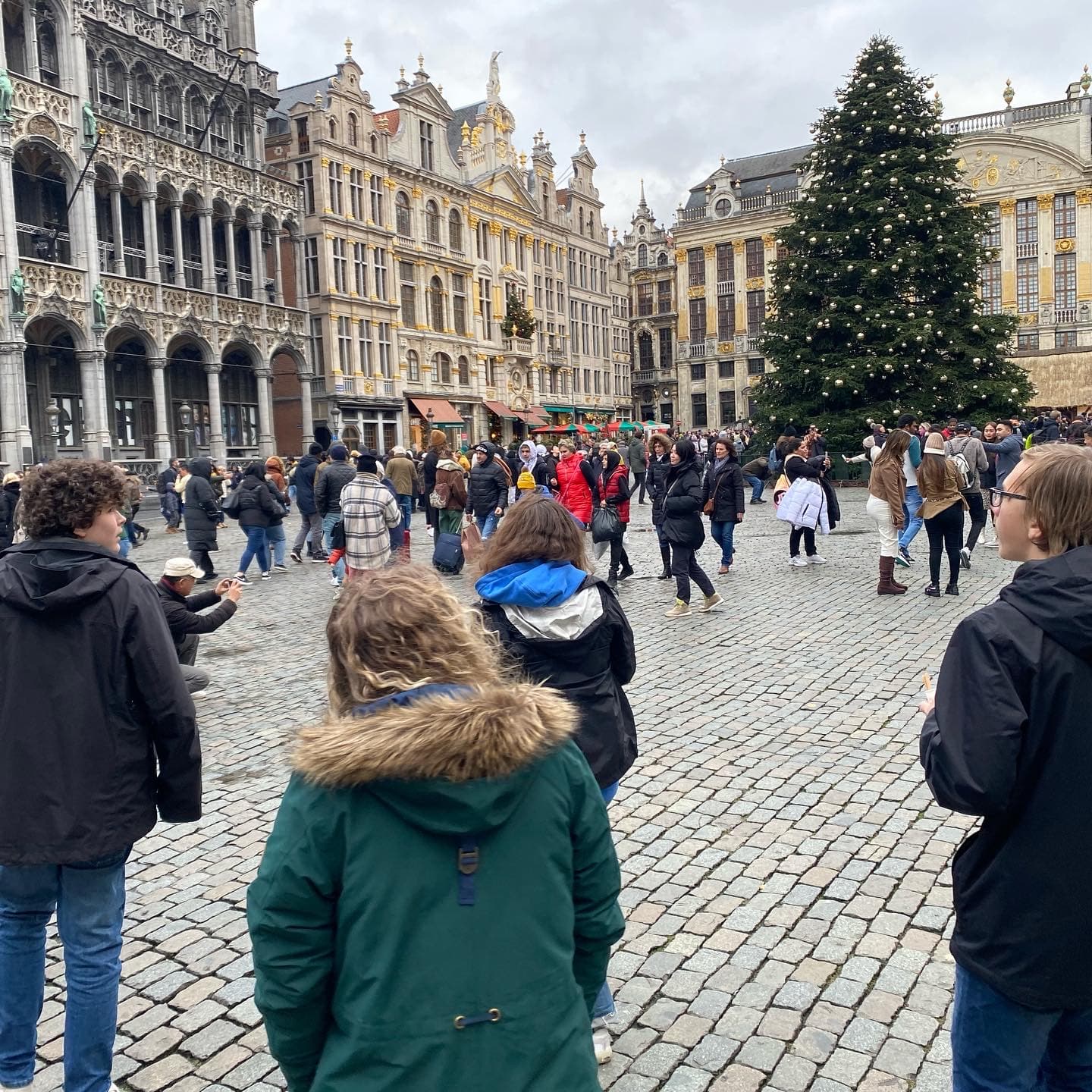 Giant outdoor Christmas tree in the center of Grand Place Plaza, Brussels, with people enjoying the scenery.
