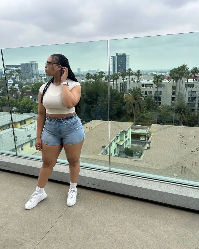 Picture of Nyjhria wearing a crop top and denim shorts in front of a glass barrier and city view