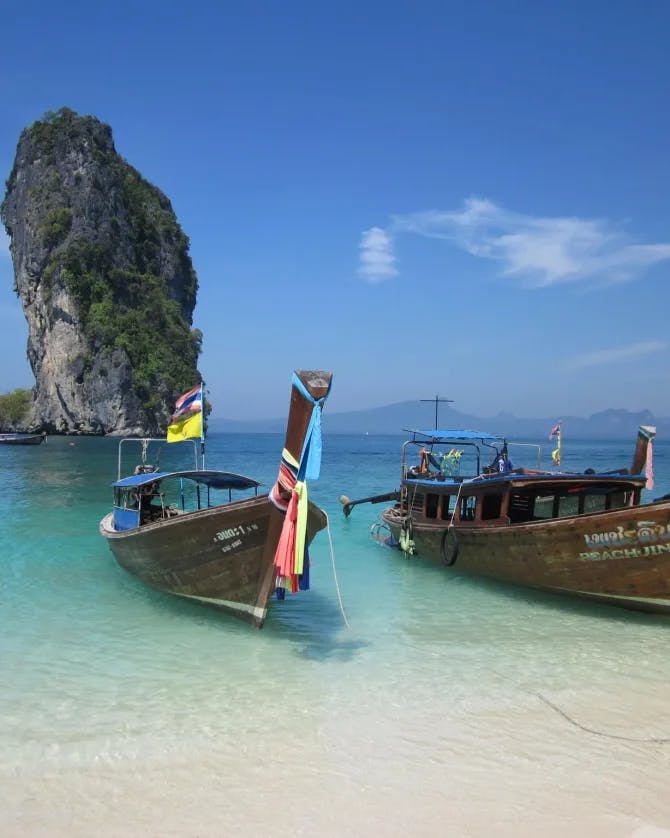 Two wooden boats anchored on a shoreline over turquoise blue water with a rock formation in the background