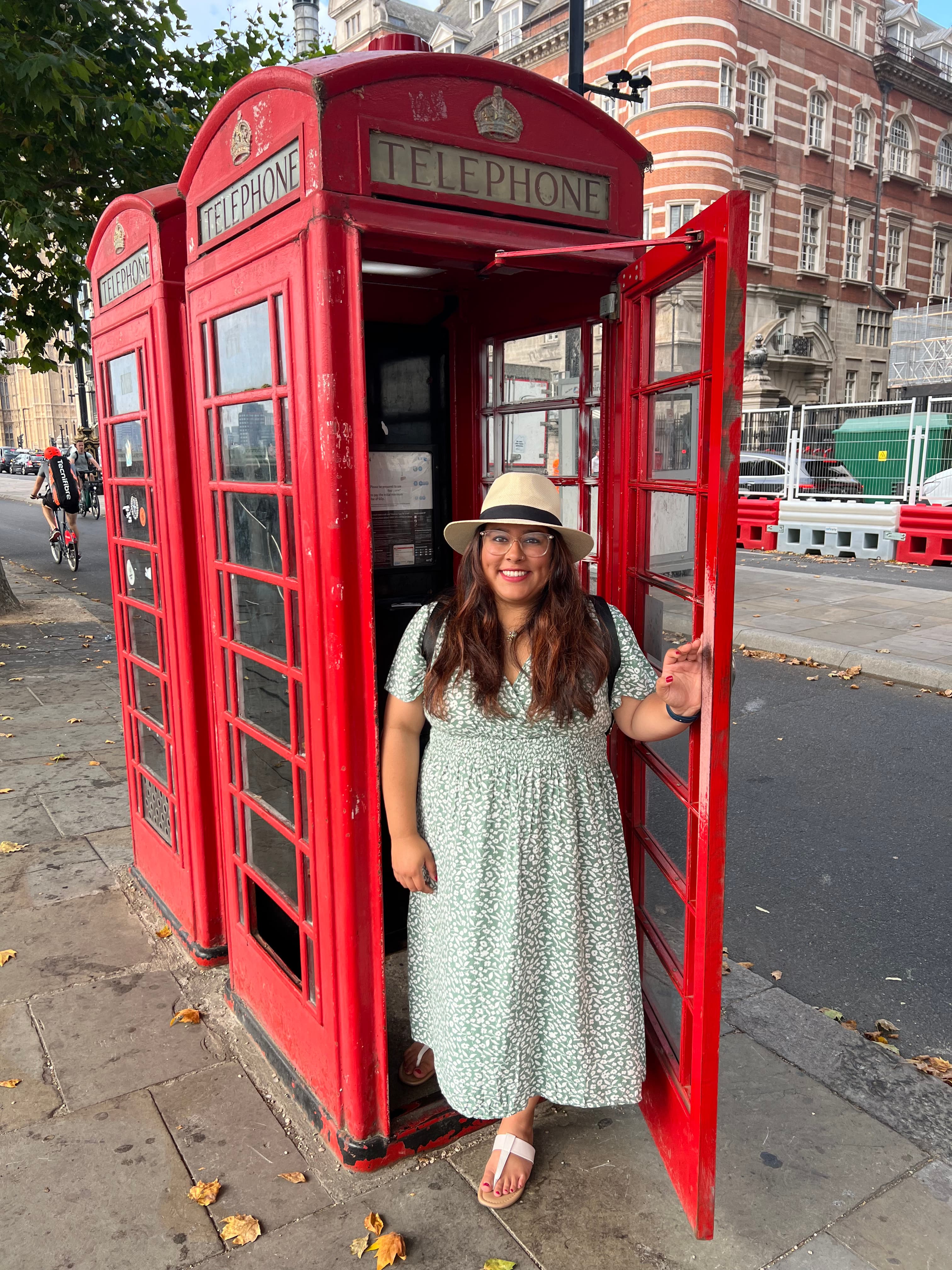 Pooja standing in the doorway of a red London-style telephone booth.