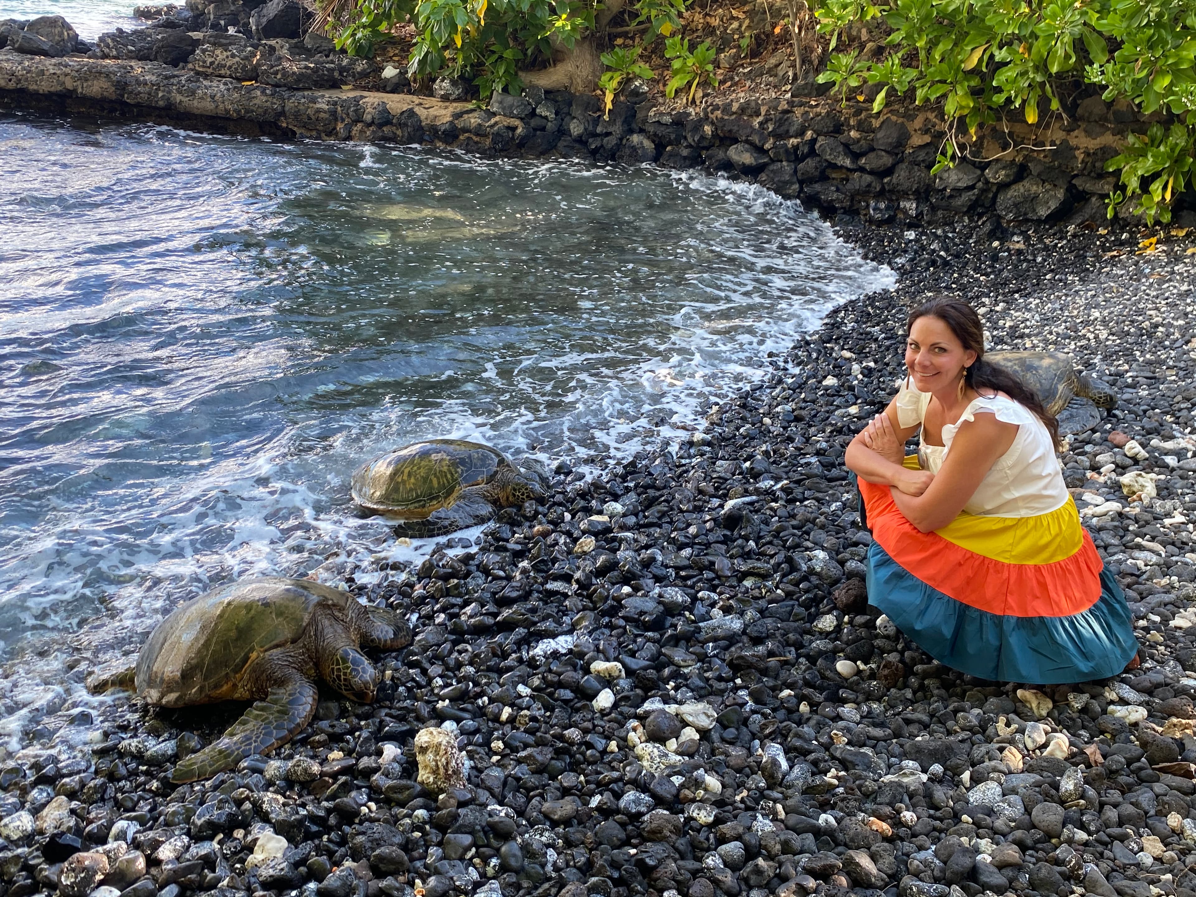 Woman posing near the shoreline with two turtles laying on the rocks.