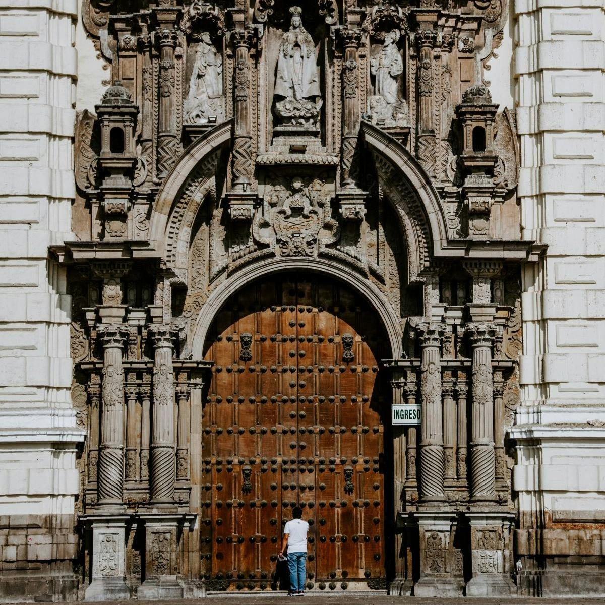 man standing near an arched wooden doorway of a regal cathedral