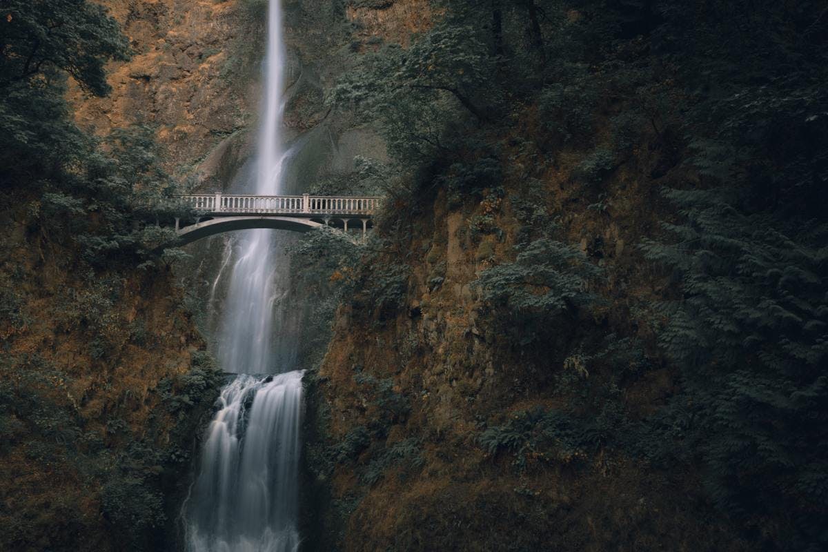 Waterfall at Columbia River Gorge in Oregon with bridge crossing over on a shady day.