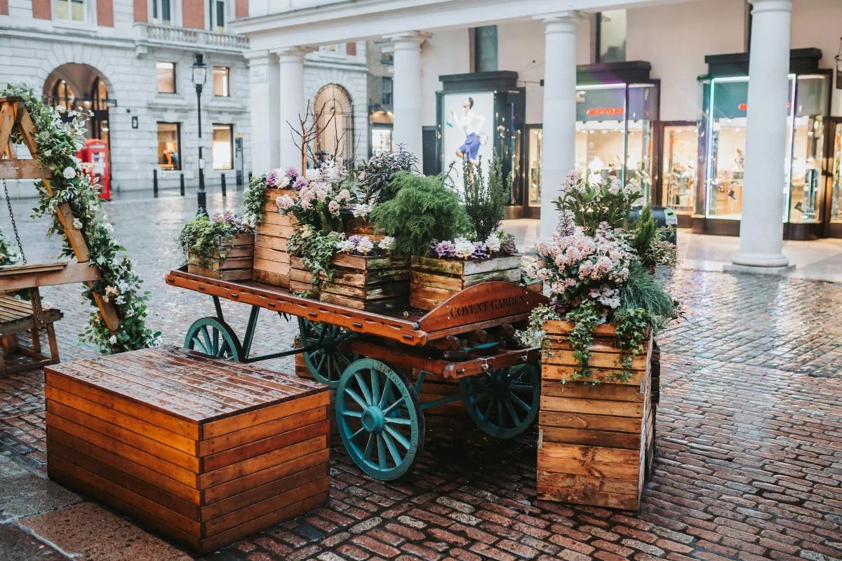A wooden cart with decorative flowers outside on a brick road with shopping centers in the background.