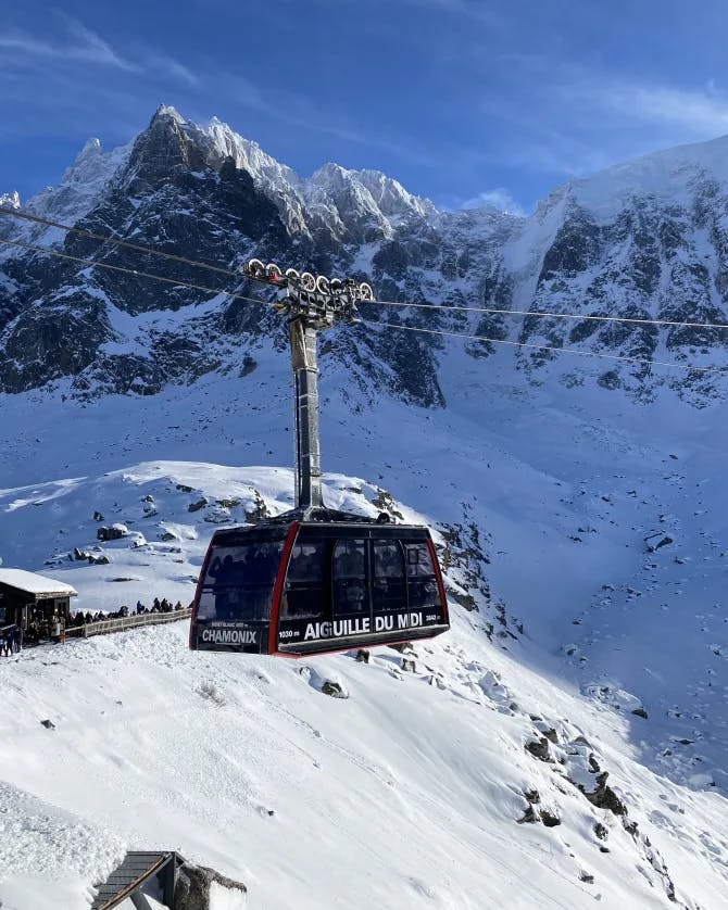 Picture of a red ski lift traveling above snowy mountains under the cloudy and blue sky