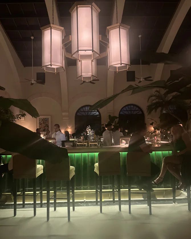 A photo of a bar with green tiling, bar stools and chandeliers hanging from the ceiling