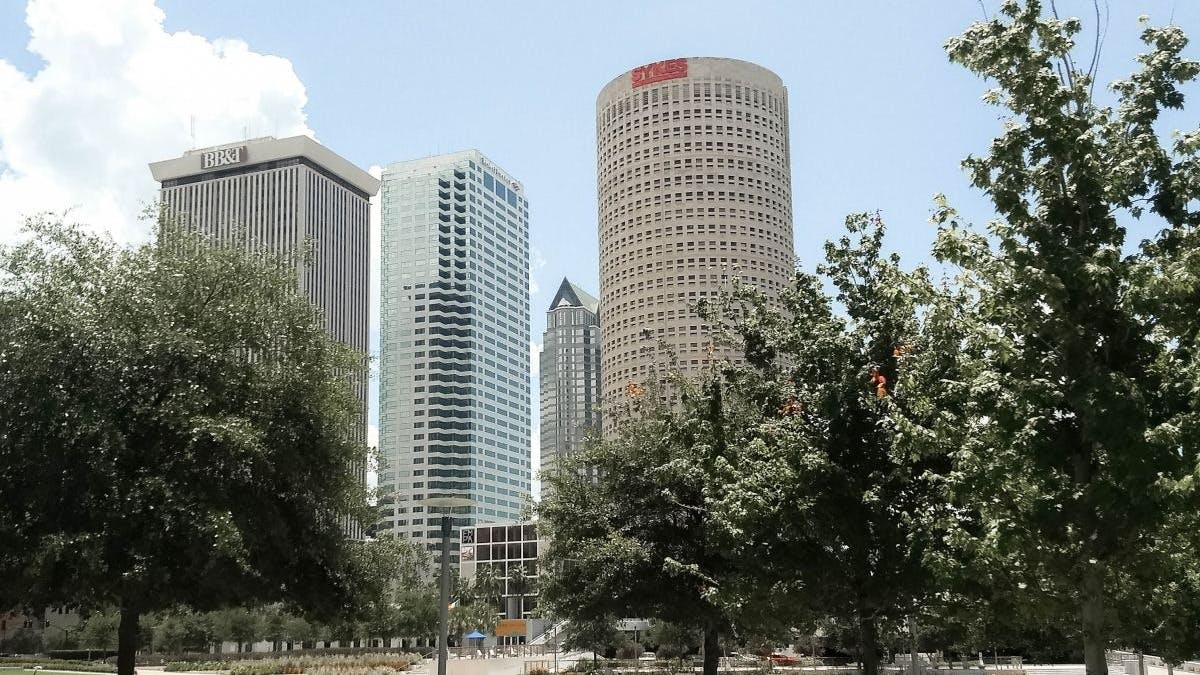 Park with green grass and trees in front of skyline of tall buildings.