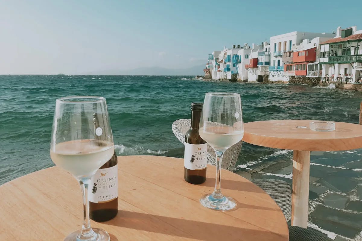 Two wine glasses with bottles on a wooden table in front of a beach during the daytime.
