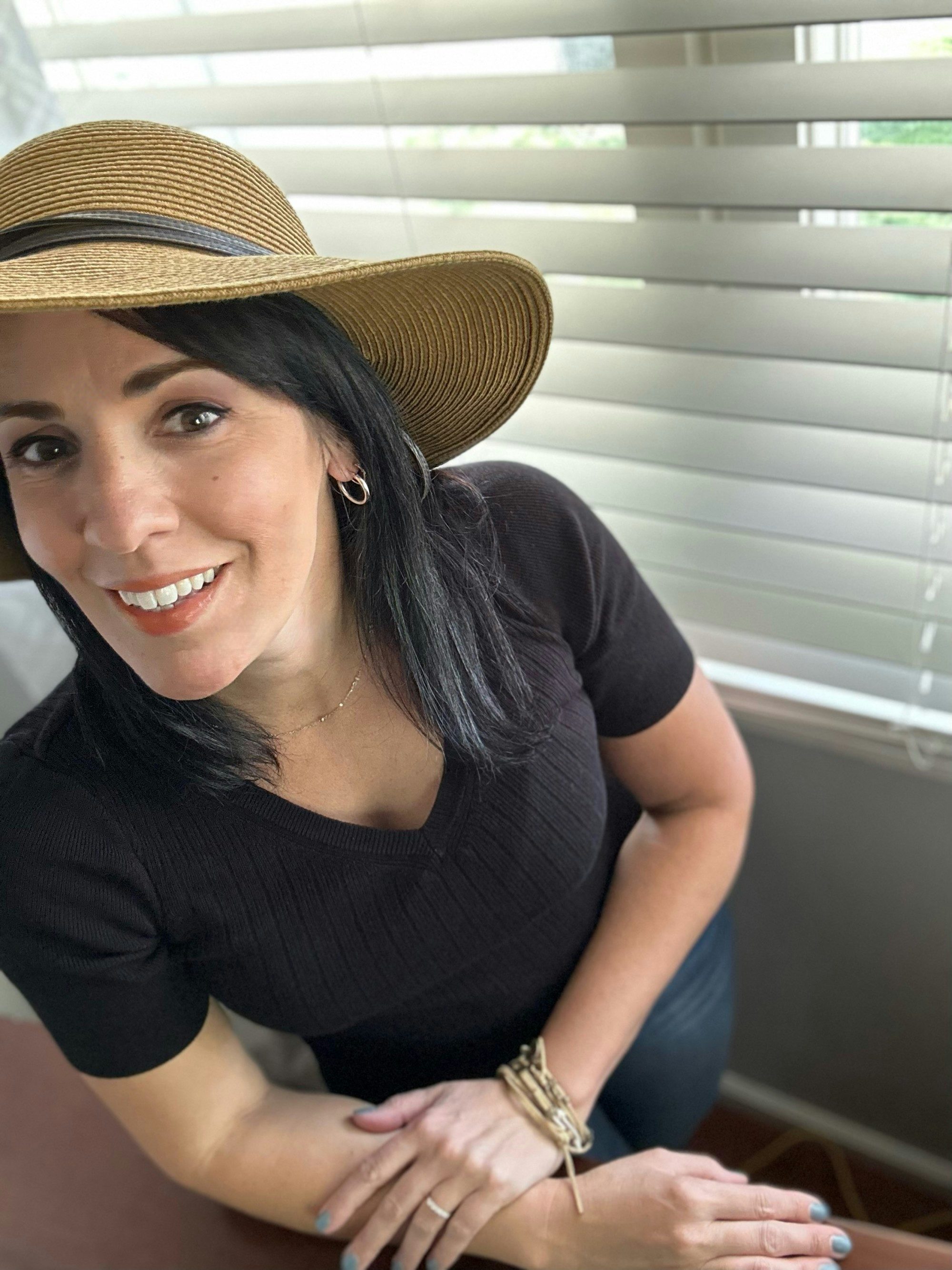 travel advisor Jennifer DiDonna in a tan hat and black shirt in front of window blinds