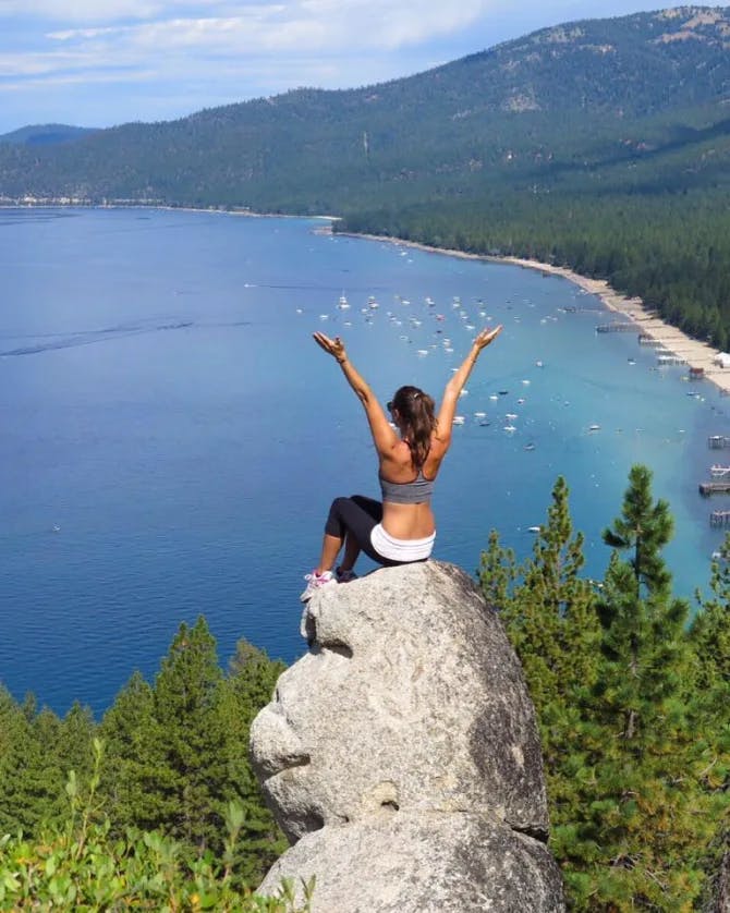 Angela sitting on Monkey Rock with her hands reaching above her head looking out onto an ocean view surrounded by green mountains