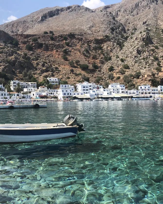 A boat floating on crystal blue water with greek buildings and a mountain in the background