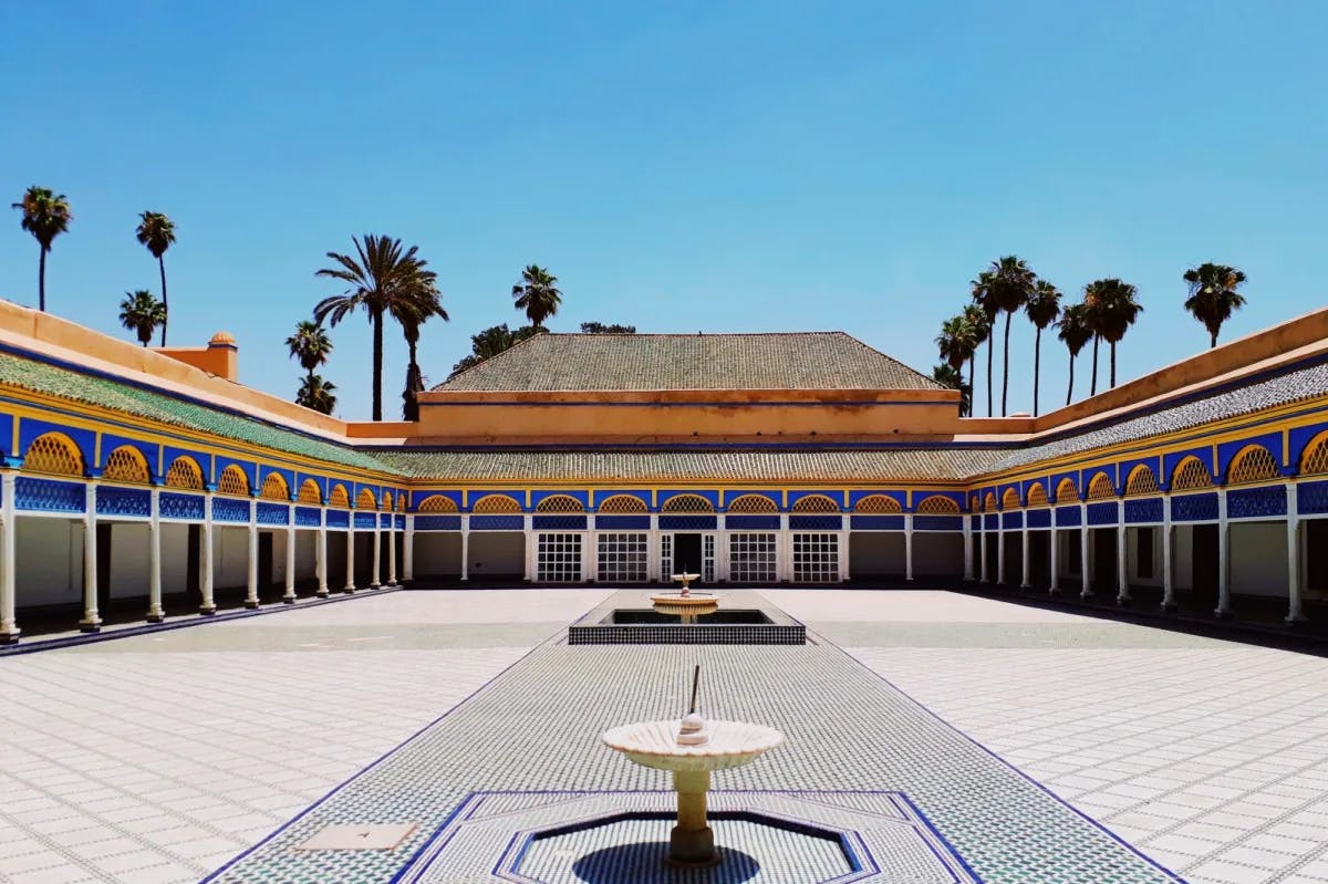 Geometric tiles surround twin fountains before ornate and colorful archways lining the walls of the Bahia Palace courtyard