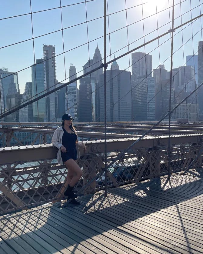 Elyssa posing on the Brooklyn bridge with the New York City skyline in the background on a sunny day