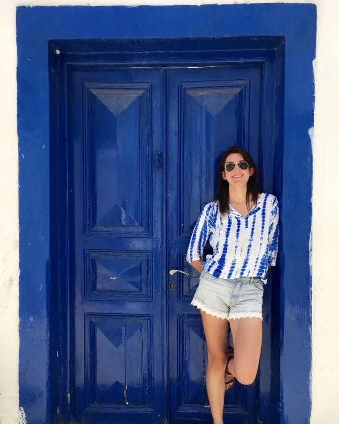 Annie wearing a blue and white top with denim shorts in front of a cobalt blue door