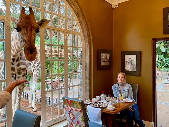 Picture of Lori sitting in a resturant with giraffe peeking inside