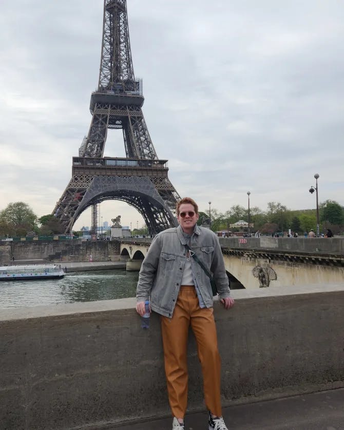 Lucas standing against a stone ledge in front of the Eiffel Tower in Paris, France