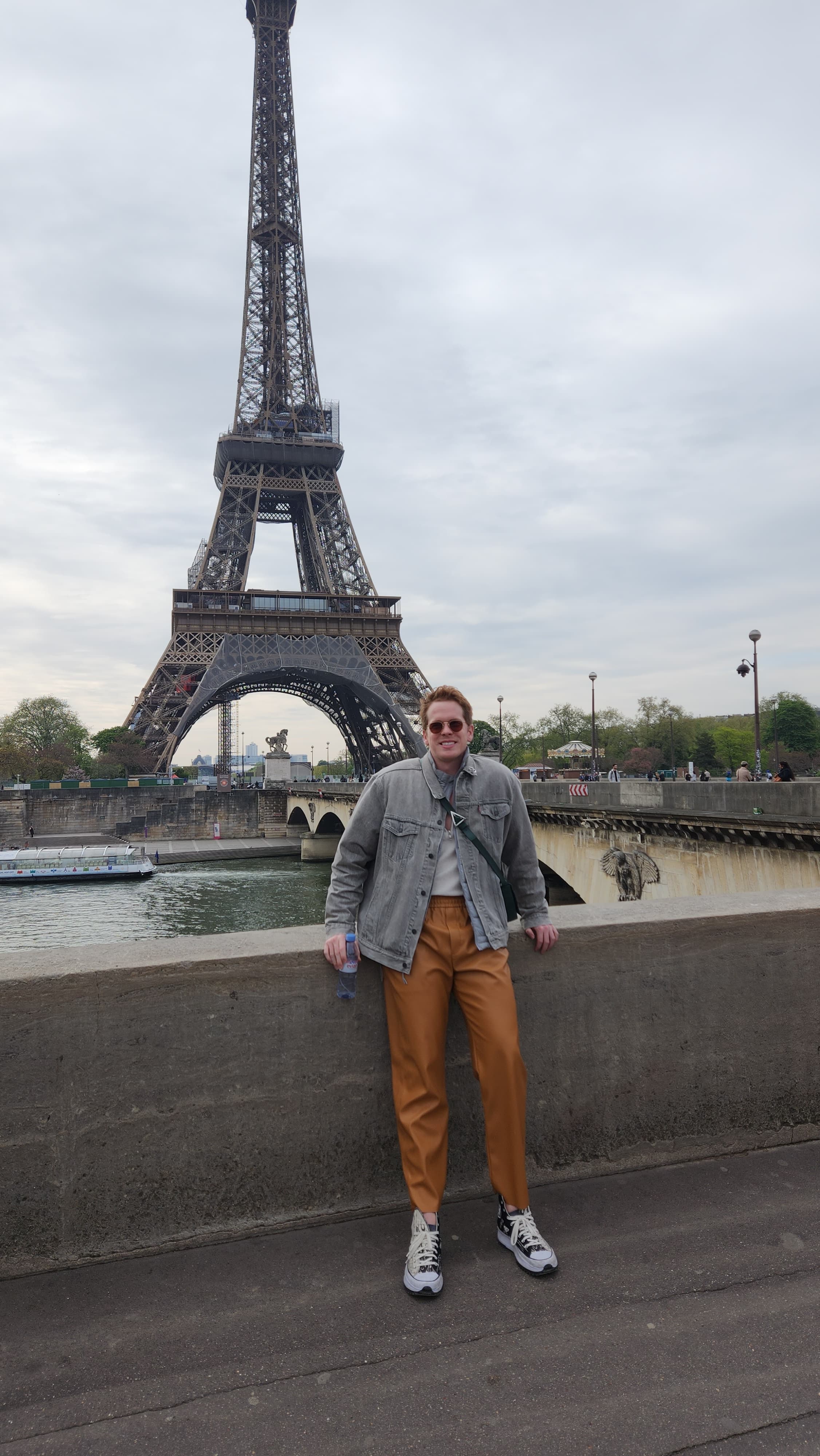 Lucas standing against a stone ledge in front of the Eiffel Tower in Paris, France