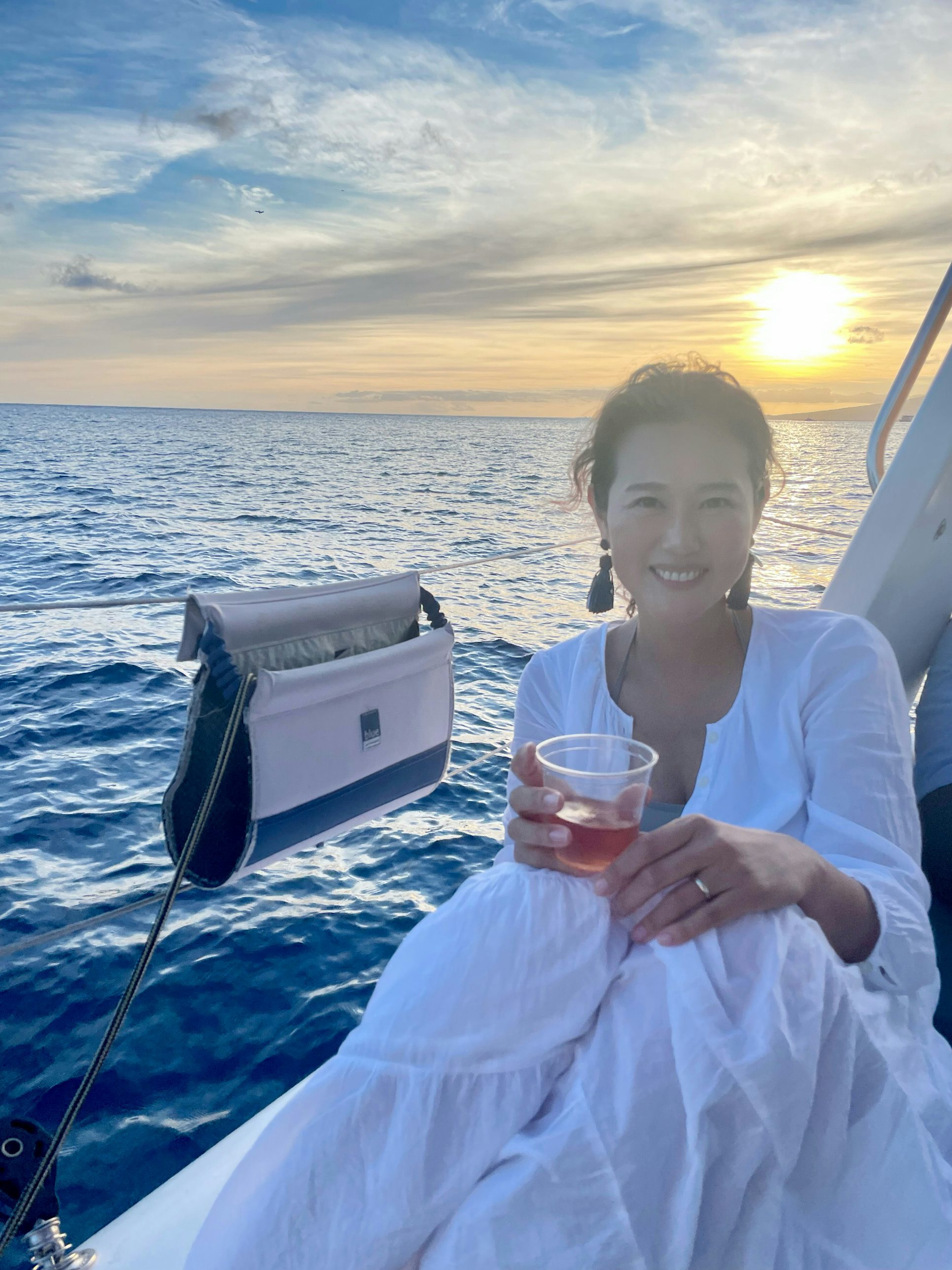 Jini Cho wearing white dress and holding drink in front of the sunset