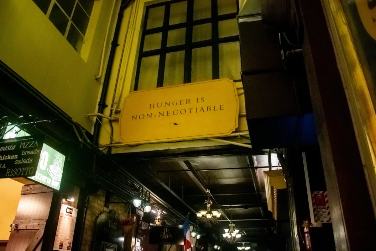 A yellow sign hanging from the side of a building at night that reads "hunger is non-negotiable". 