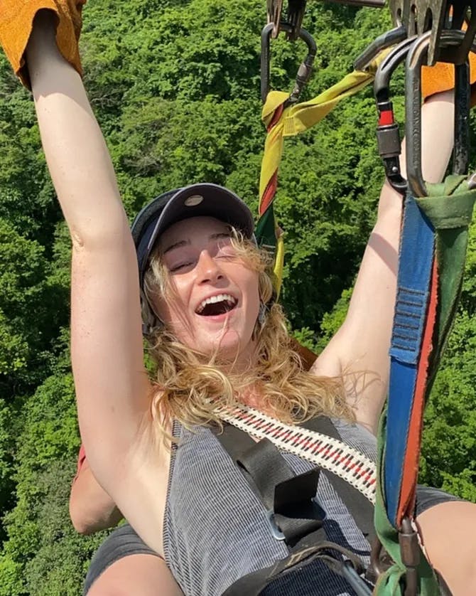 A thrilling zip-lining experience with trees in the background and Emily's hands raised in the air