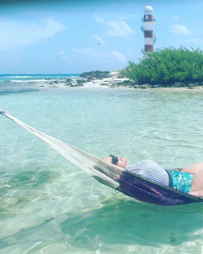 Picture of Nicole relaxing in hammock strung above crystal clear water ocean water.
