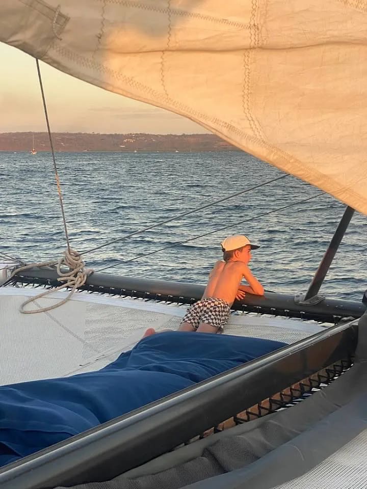 A boy on a catamaran overlooking the water at sunset.