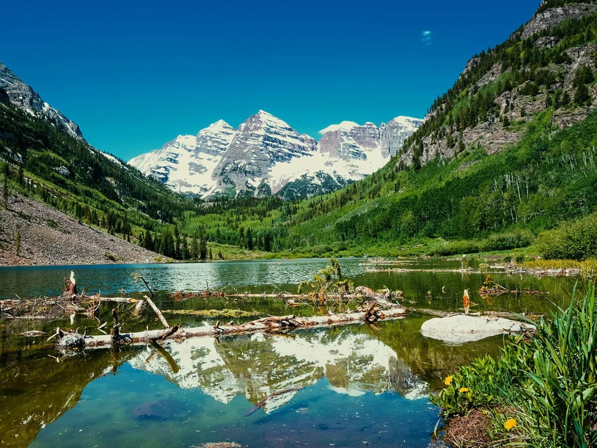 A tranquil view of a mountain lake, with snow-capped peaks reflecting in the still waters under a clear blue sky.